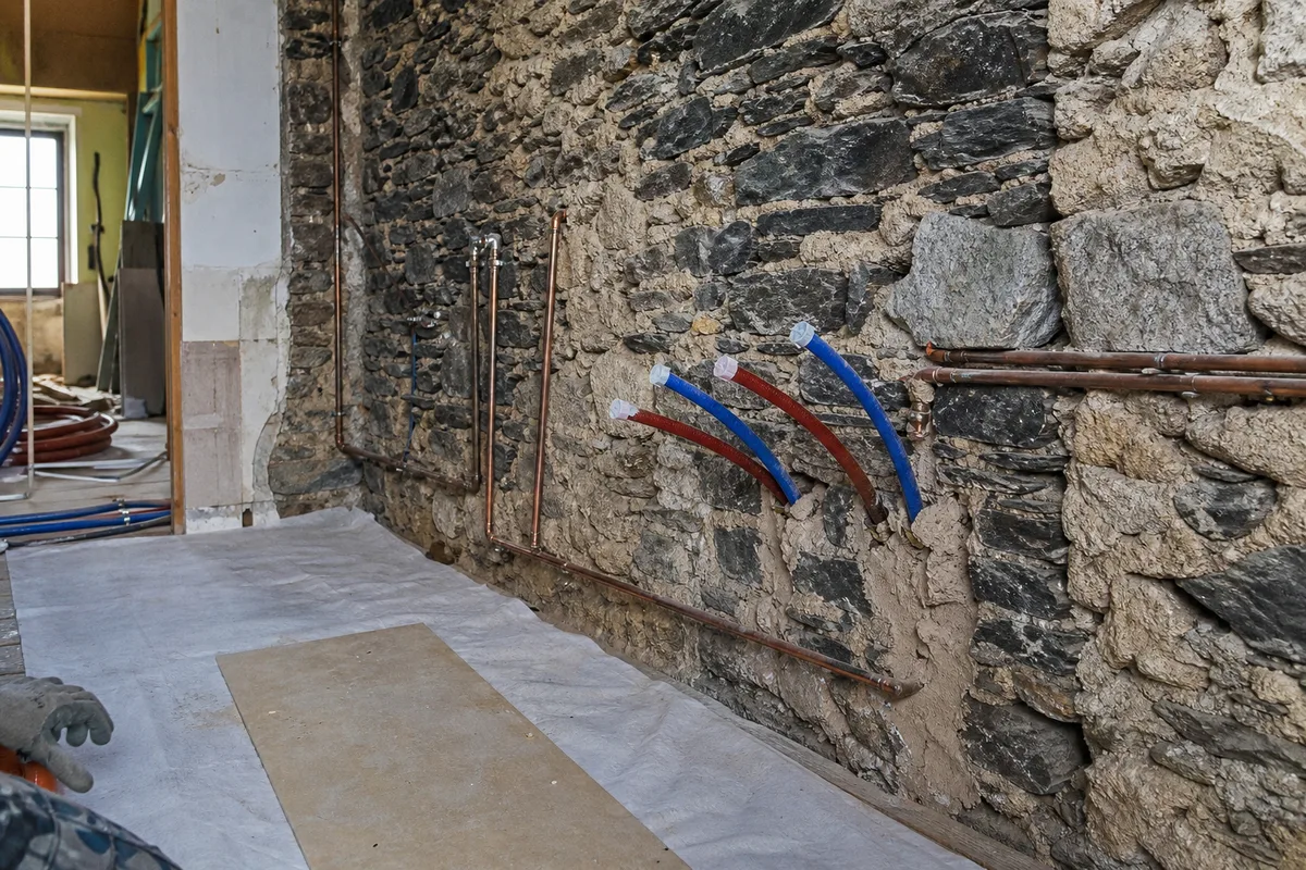 Salle de bain en rénovation dans une maison de bourg, mur en schiste apparent et réseaux plomberie en attente, lumière de chantier